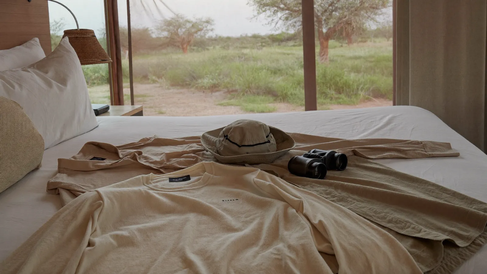 Abbigliamento da safari in colori neutri con cappello e binocolo su un letto di lodge