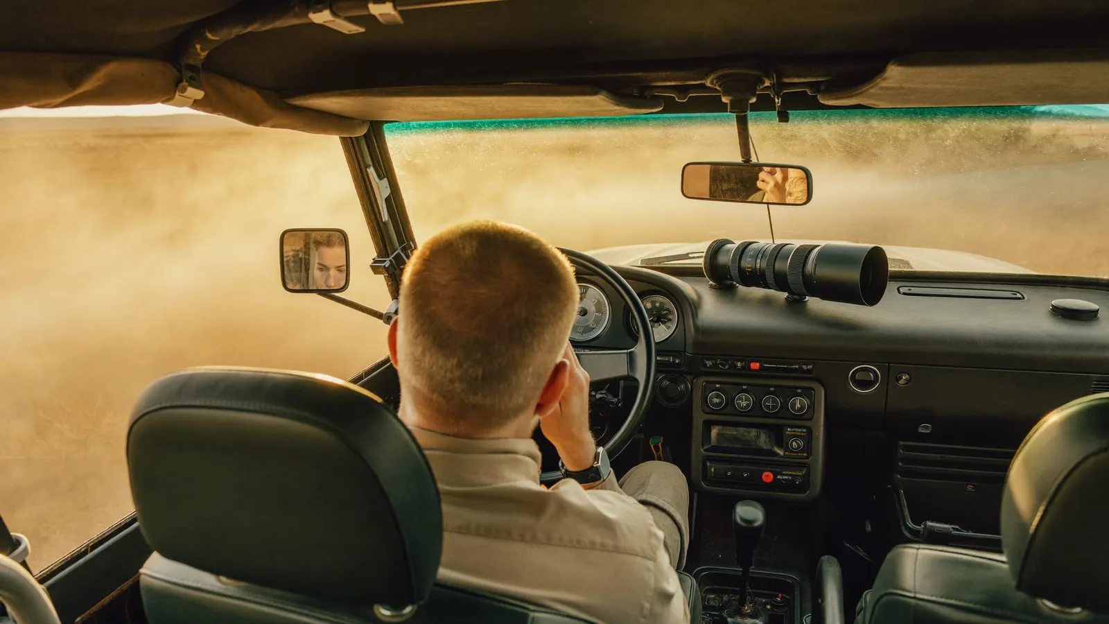 Fotografo con teleobiettivo appoggiato al tettuccio aperto di una jeep da safari al tramonto